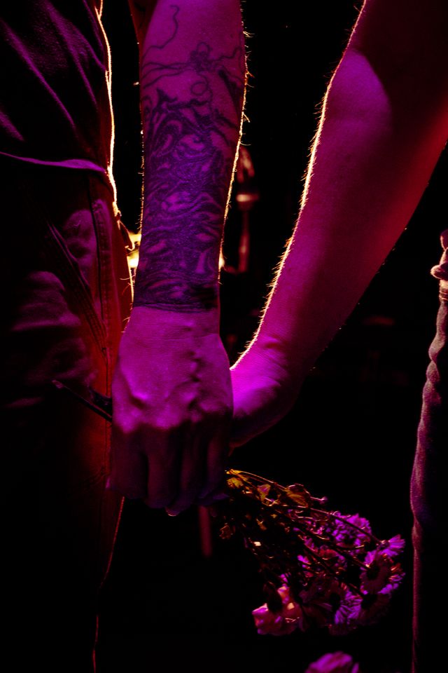 Two people holding hands and a bundle of flowers between them, backlit