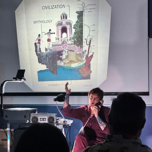 Miriam sitting next to the AV cart, talking on a (landline) phone, and gesturing. The overhead projector shows a slide with photos from Casa Bonita