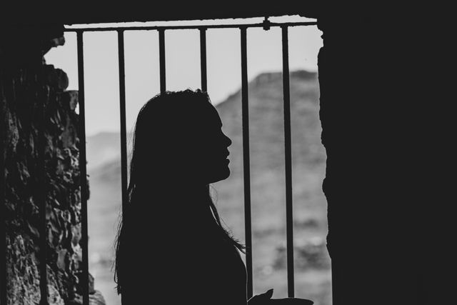 Silhouette of a woman in front of a barred window through which we see a mountain