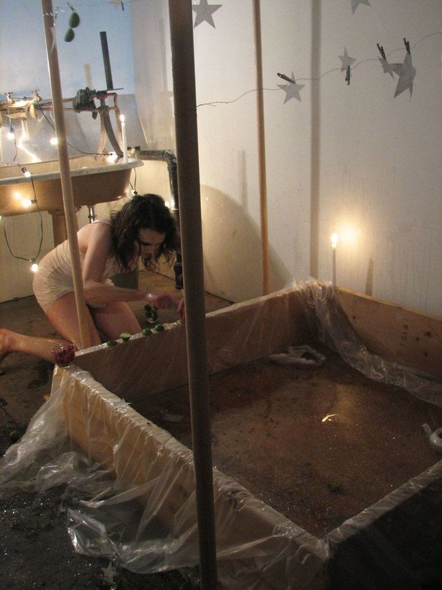 Julie in a white slip in kneeling in front of a paint sink, lining up figures on the edge of a plastic-lined mud box