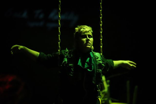 Al as a bower bird, dancing on a swing, arms wide in green light