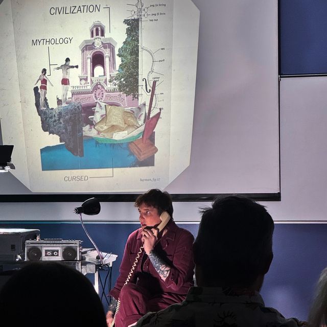 Miriam sitting next to the AV cart, talking on a (landline) phone. She seems concerned. The overhead projector shows a slide with photos from Casa Bonita