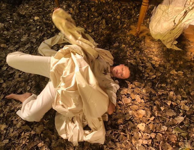 Julie on her back in a pile of leaves, with a white sheet tangled over her